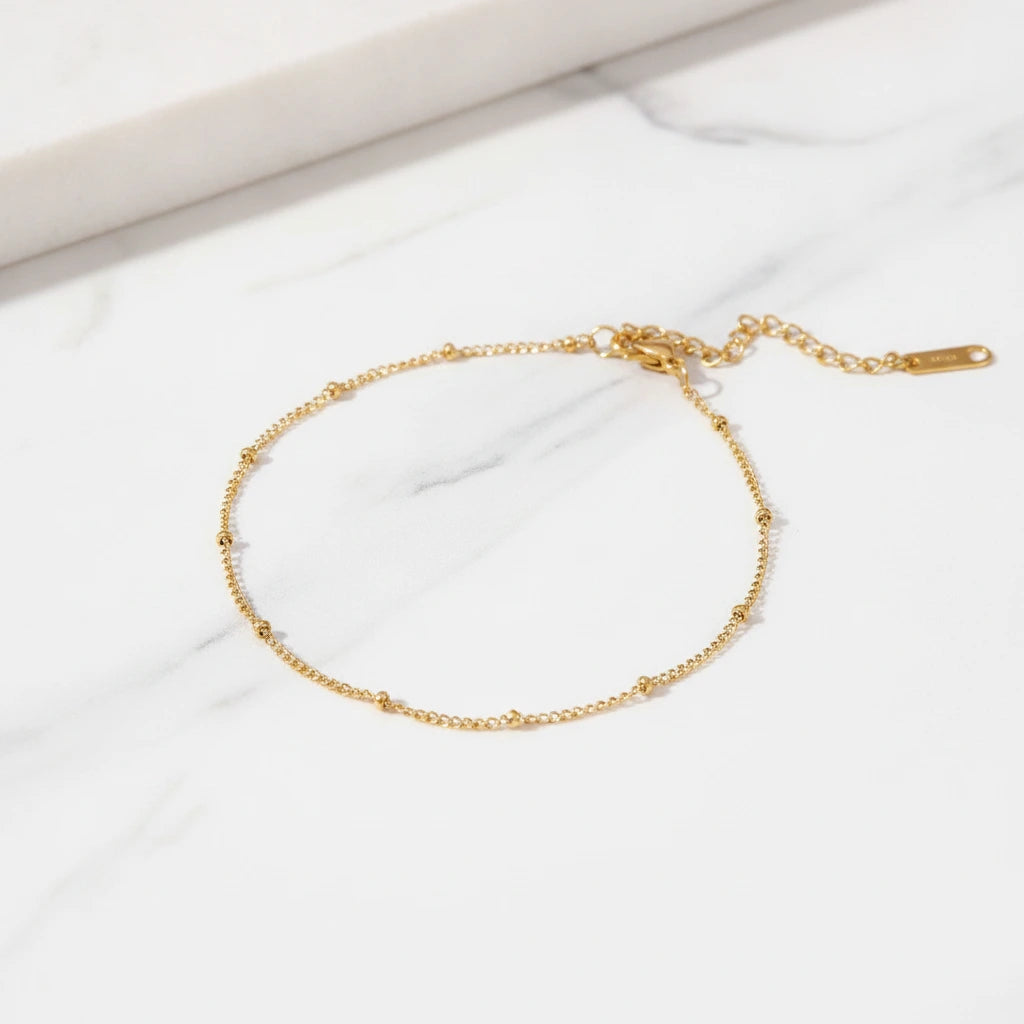 AMALFI ANKLET | Place the original product large and centered on a clean white marble surface with a matching white marble background.