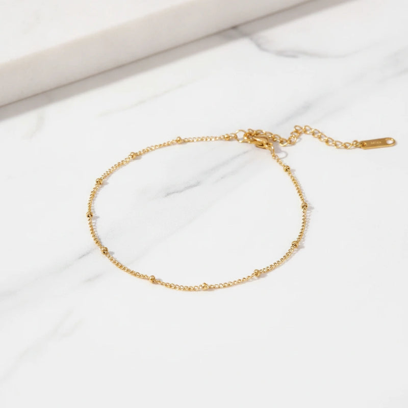 AMALFI ANKLET | Place the original product large and centered on a clean white marble surface with a matching white marble background.