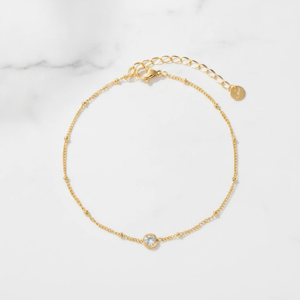 DAINTY ANKLET | Place the original product large and centered on a clean white marble surface with a matching white marble background.